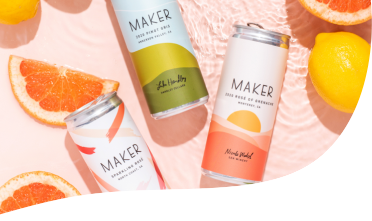 Three Maker Wine cans sitting in shallow water alongside grapefruit, lemons, and limes.