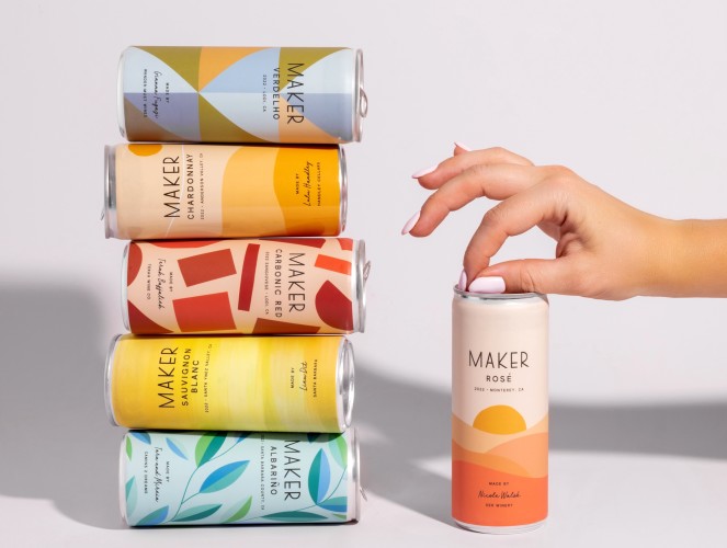 Cans of Maker Wine stacked on top of one another with a hand cracking one can open