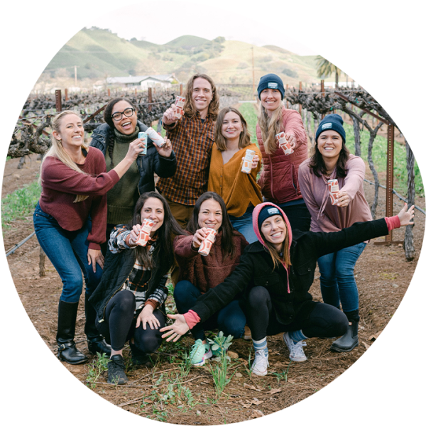 The entire Maker Wine team holding cans in a vineyard.