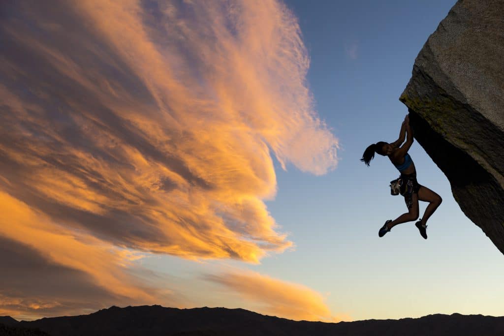 a woman hanging off a rock free climbing