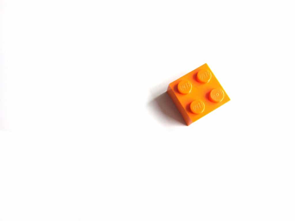 an orange 2 by 2 piece of lego on a white surface