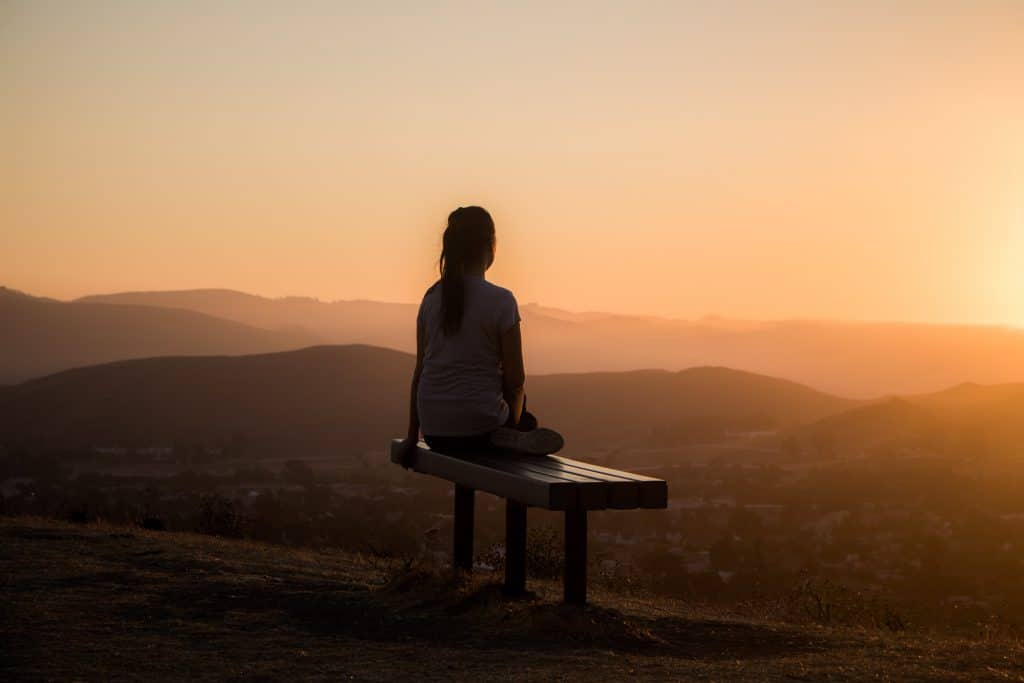 a girl on a bench looking over a hillscape