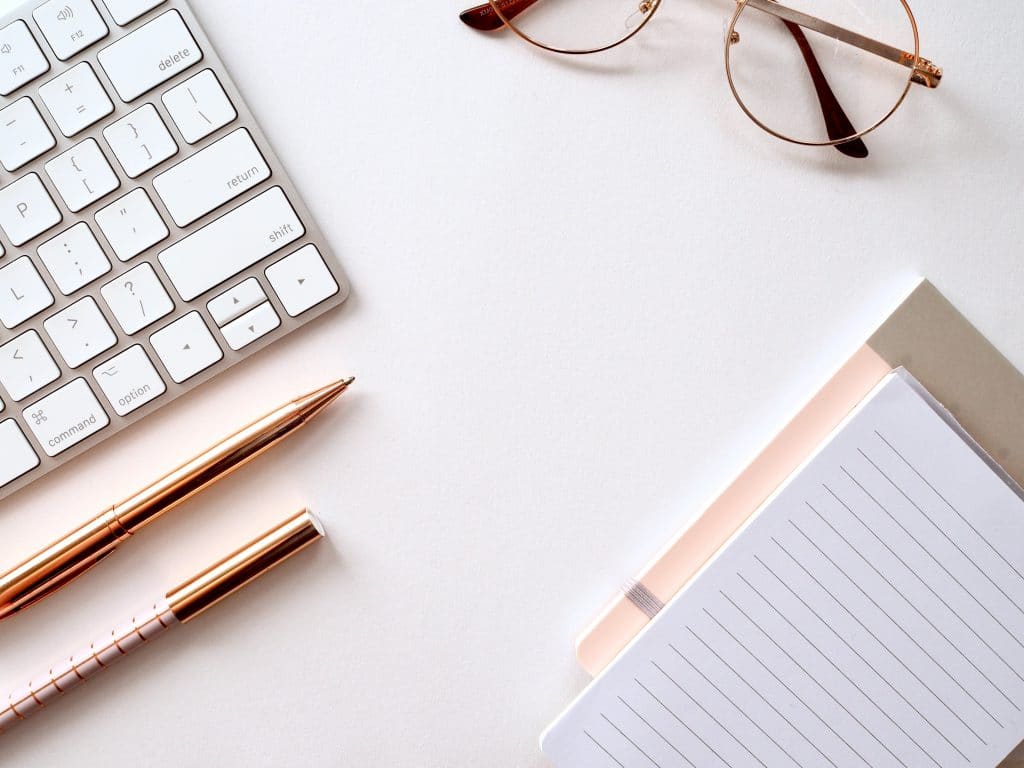 pens, notebook, glasses and keyboard on a desk