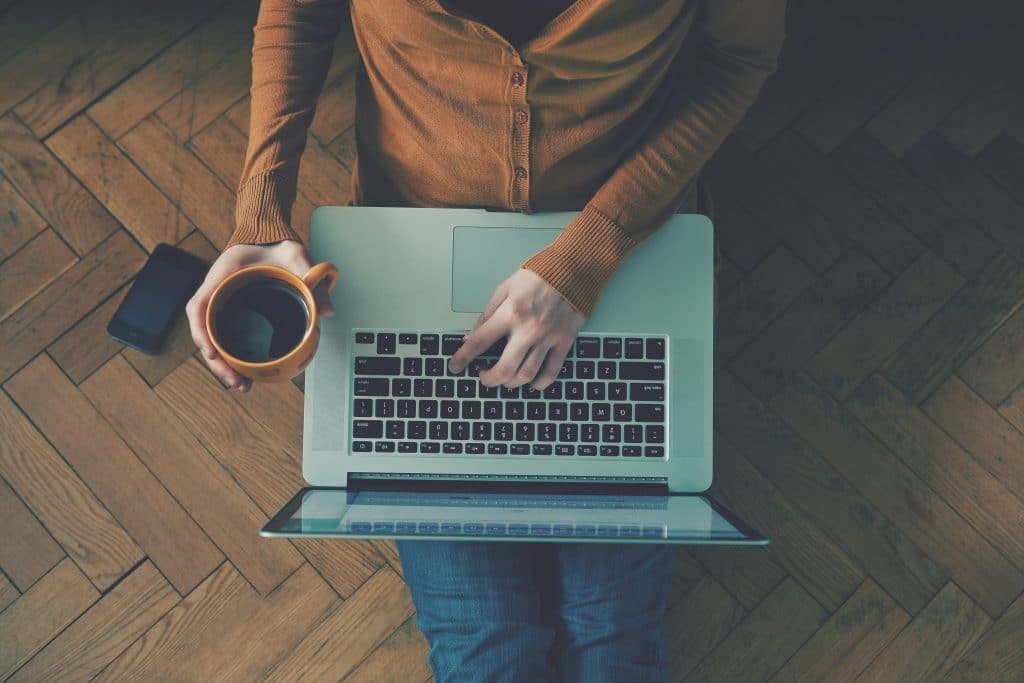 a man sitting on the floor with his laptop and a coffee