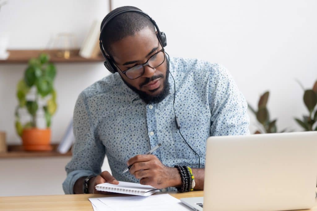 a man listening to a laptop and taking notes