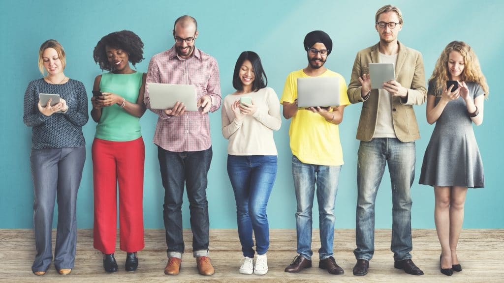 7 people standing in a line using various devices