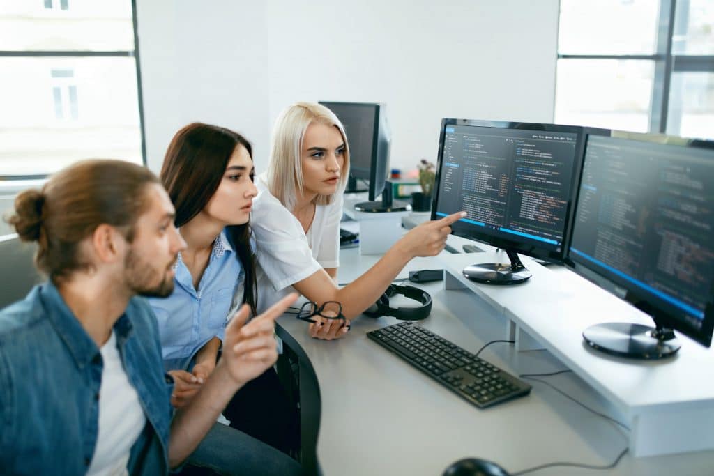 3 people discussing sowftware code on computer monitors