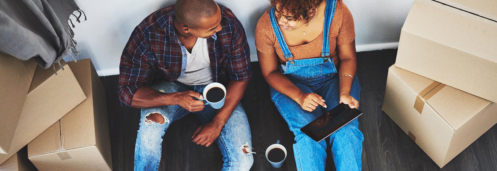 2 people sat on the floor drinking coffee with boxes around them