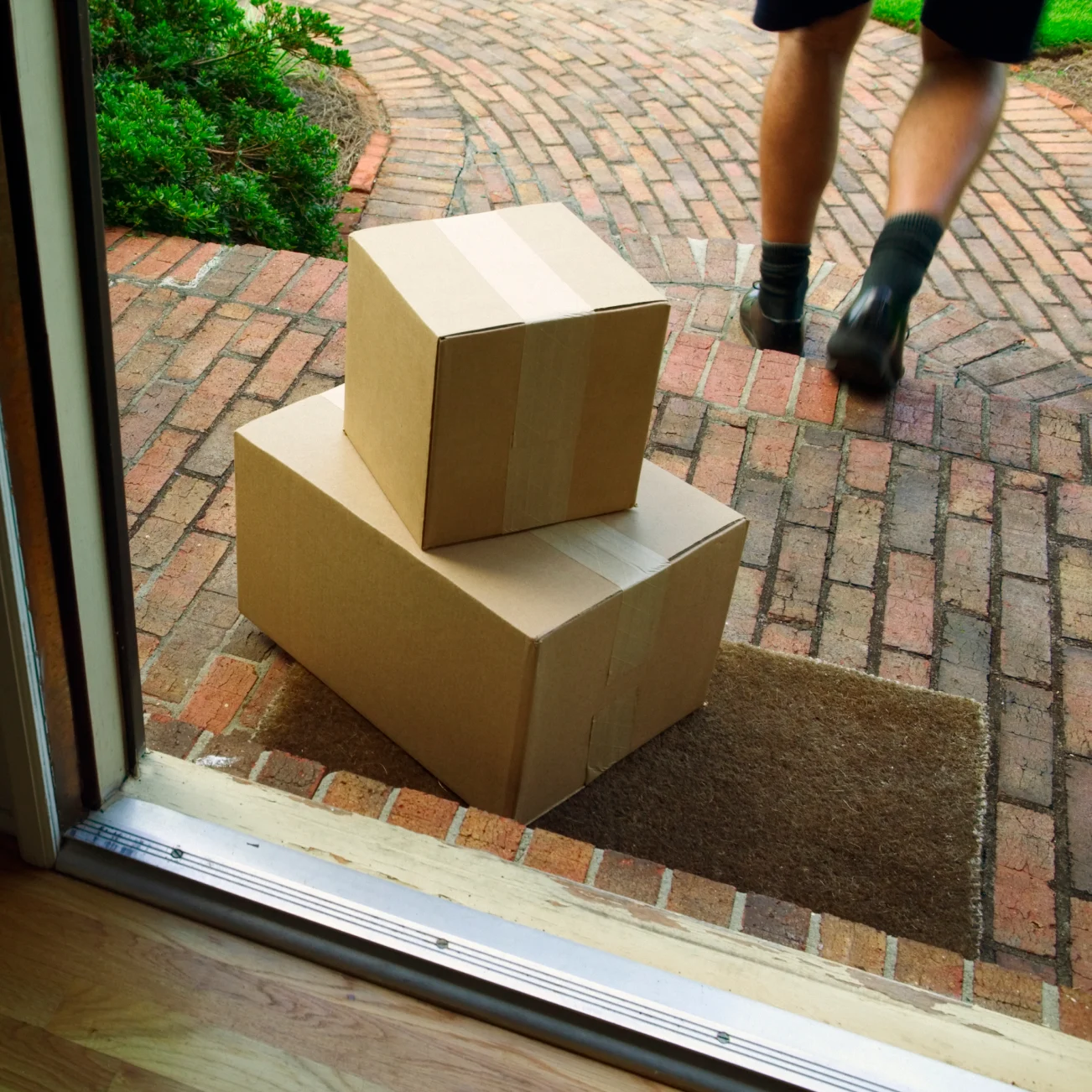 2 boxes on doormat seen through an open door with delivery driver walking away