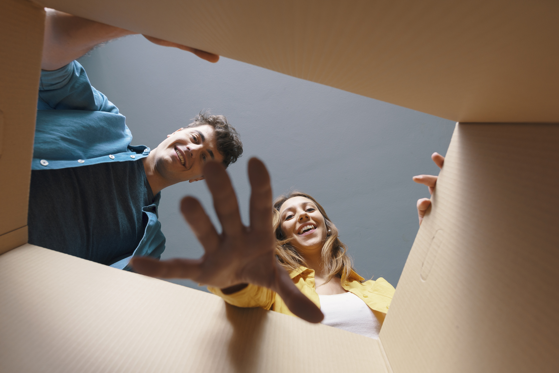 Male and female presenting people reach into a cardboard box, reaching towards the camera.