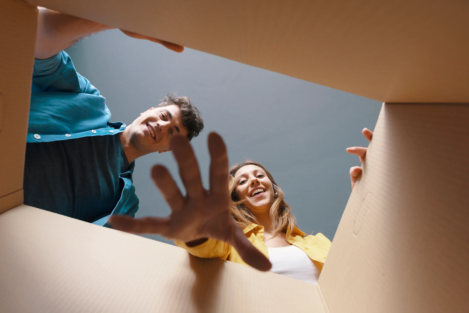 Male and female presenting people reach into a cardboard box, reaching towards the camera.