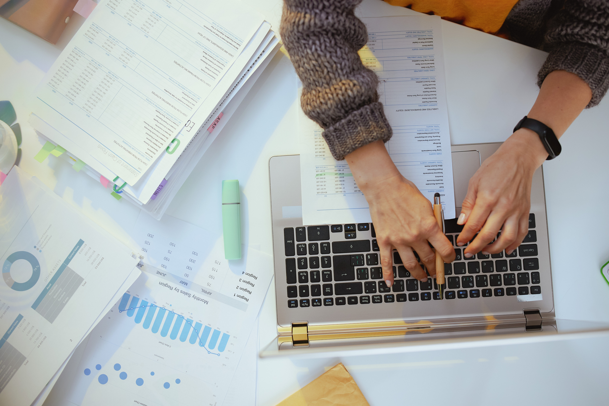 Hands typing at a laptop, surrounded by graphs and papers.