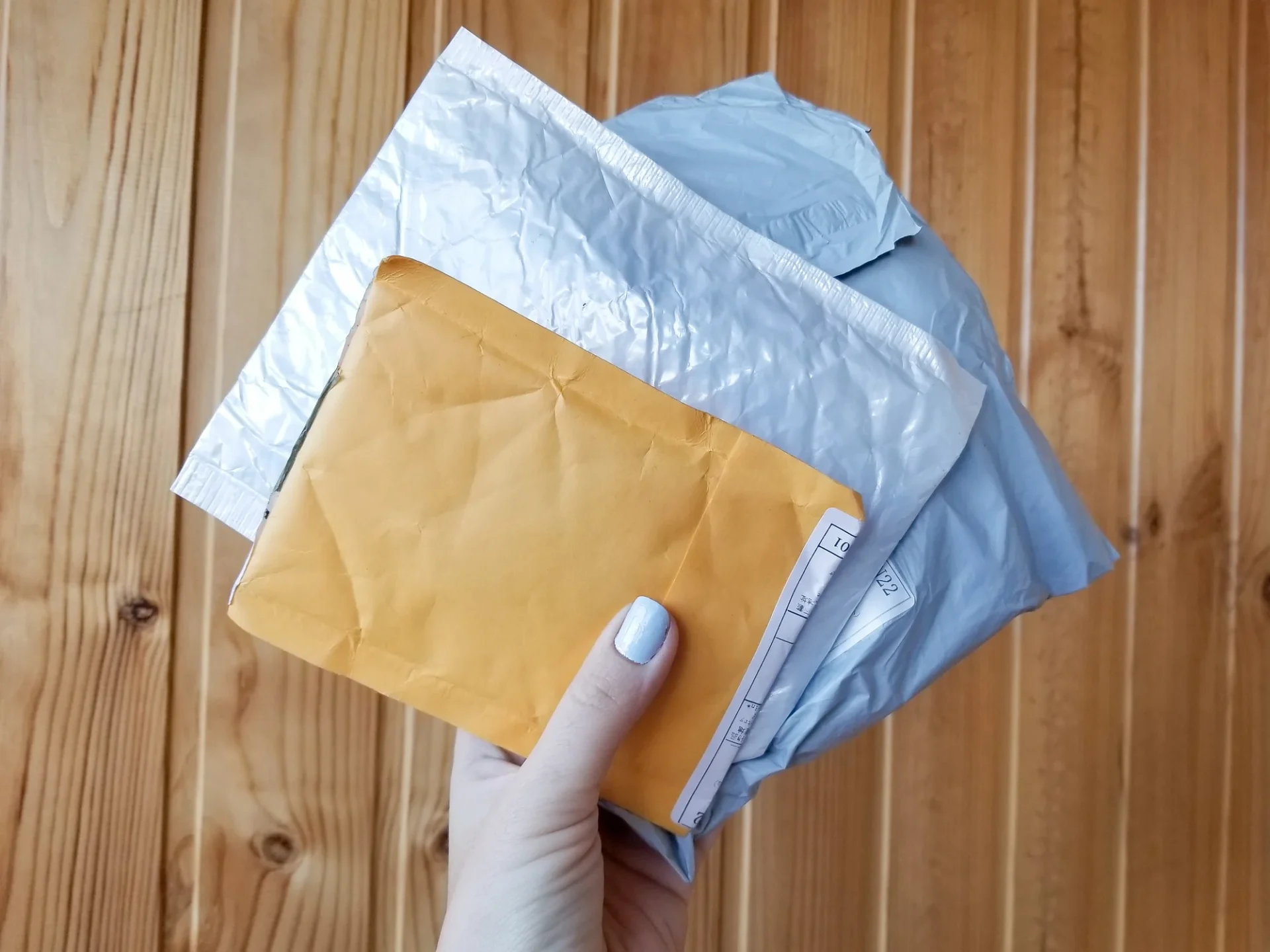 Woman's hand holding 3 postable sized parcels in envelope and silver packaging