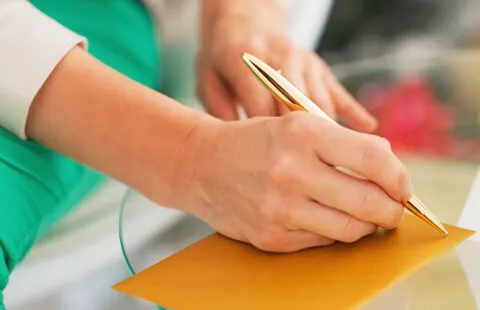 Woman signing a card-sized envelope with a gold pen