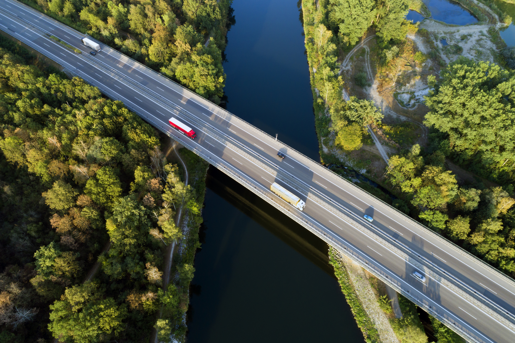 Ariel view of lorries on a highway over a river and trees.