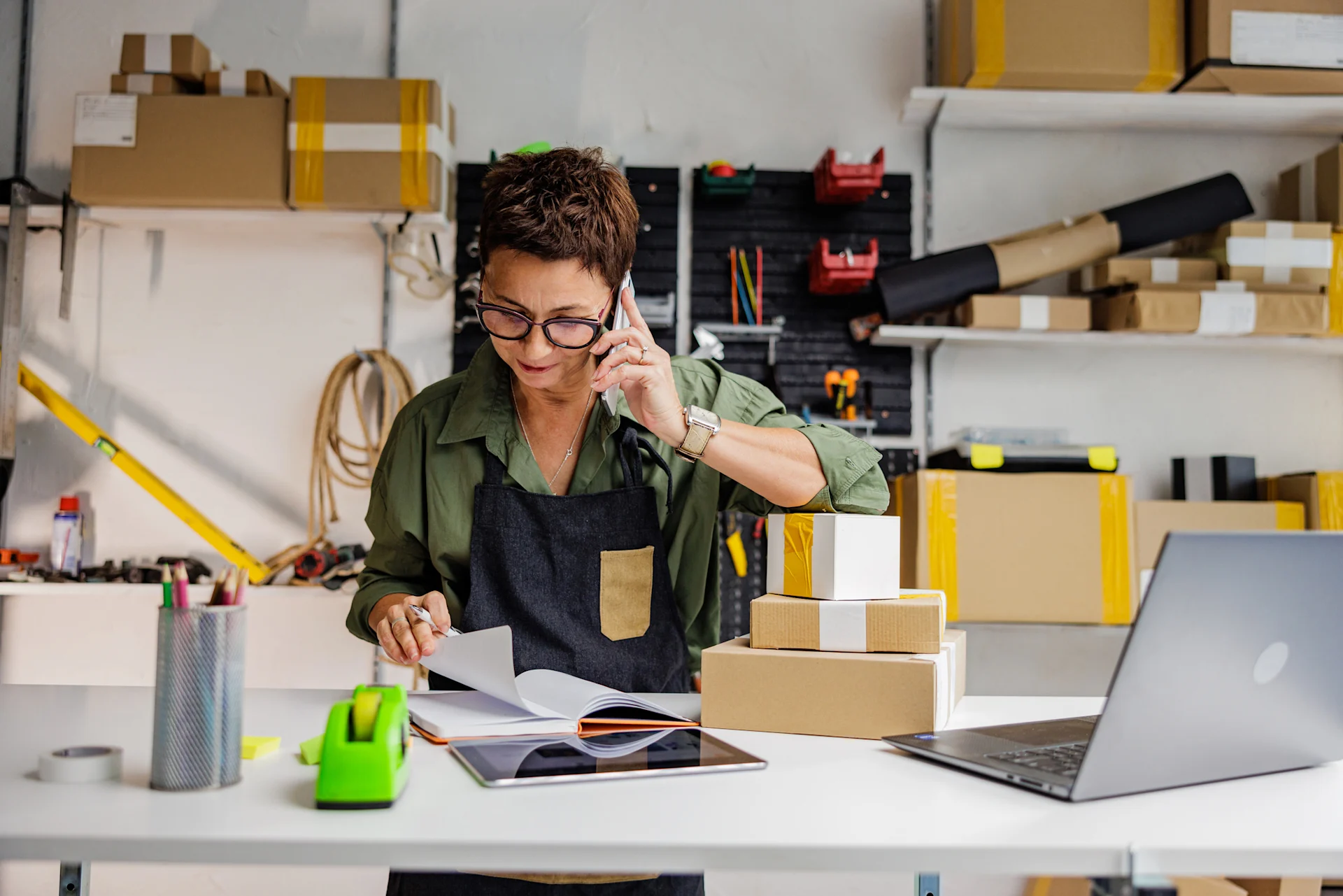 Female presenting person speaks on the phone in her workshop, looking at documents on the table.