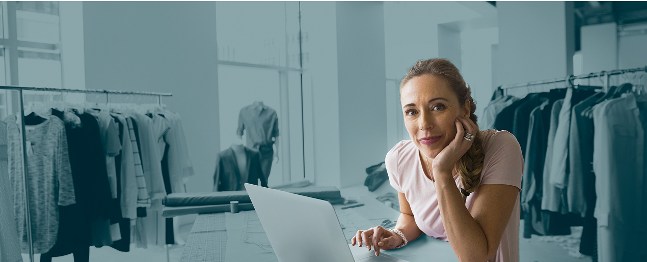 Woman on laptop at home with clothes business in background