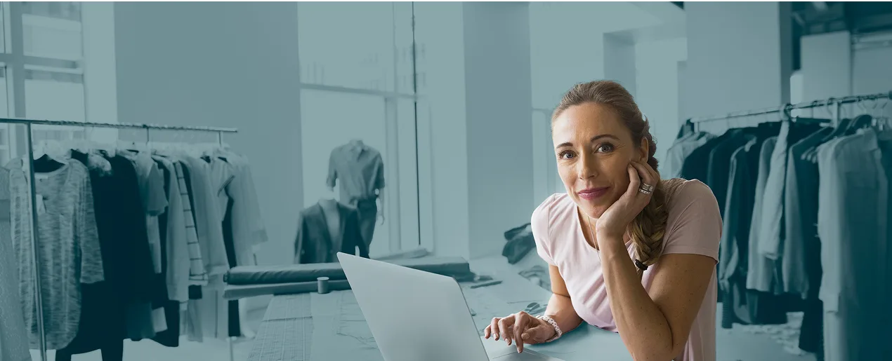 Woman on laptop at home with clothes business in background