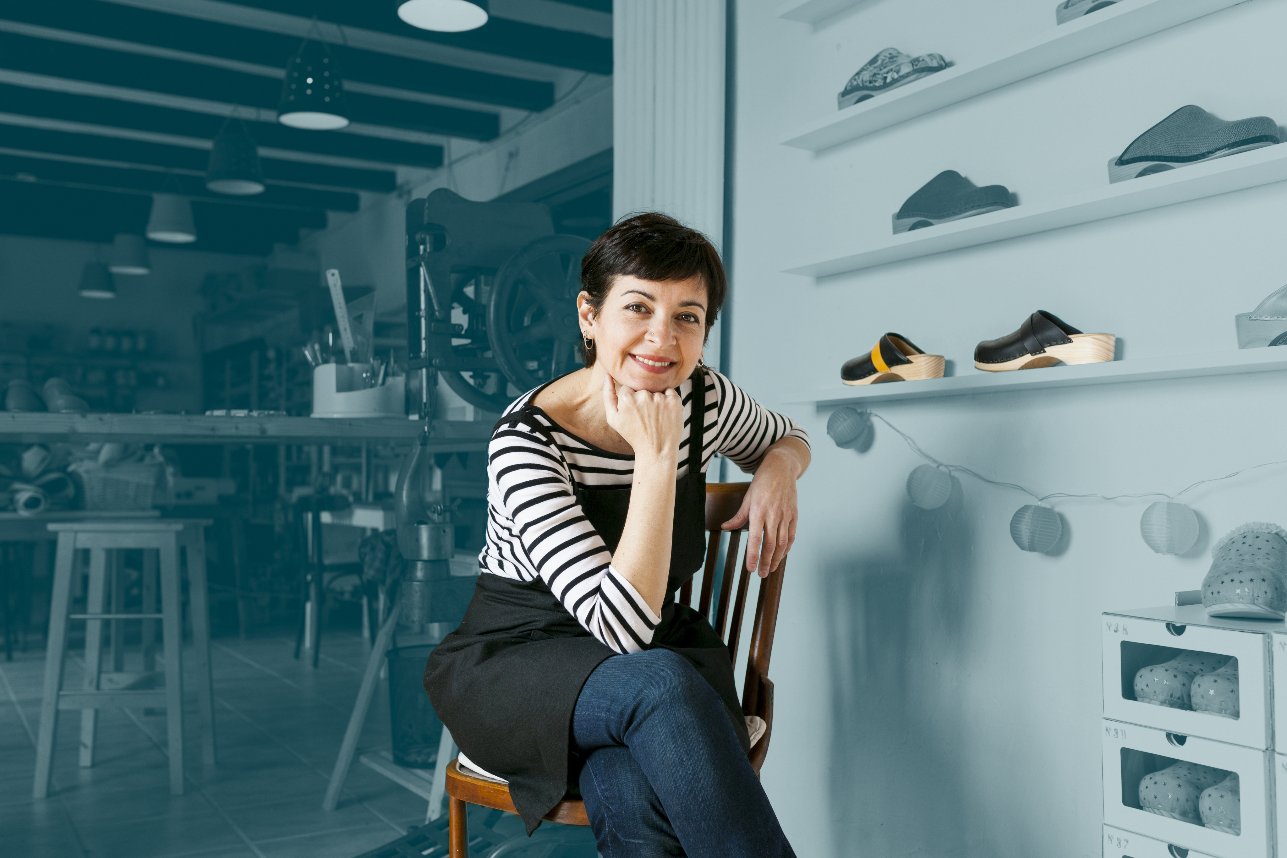Woman sat by a shoe shelf in her store. 