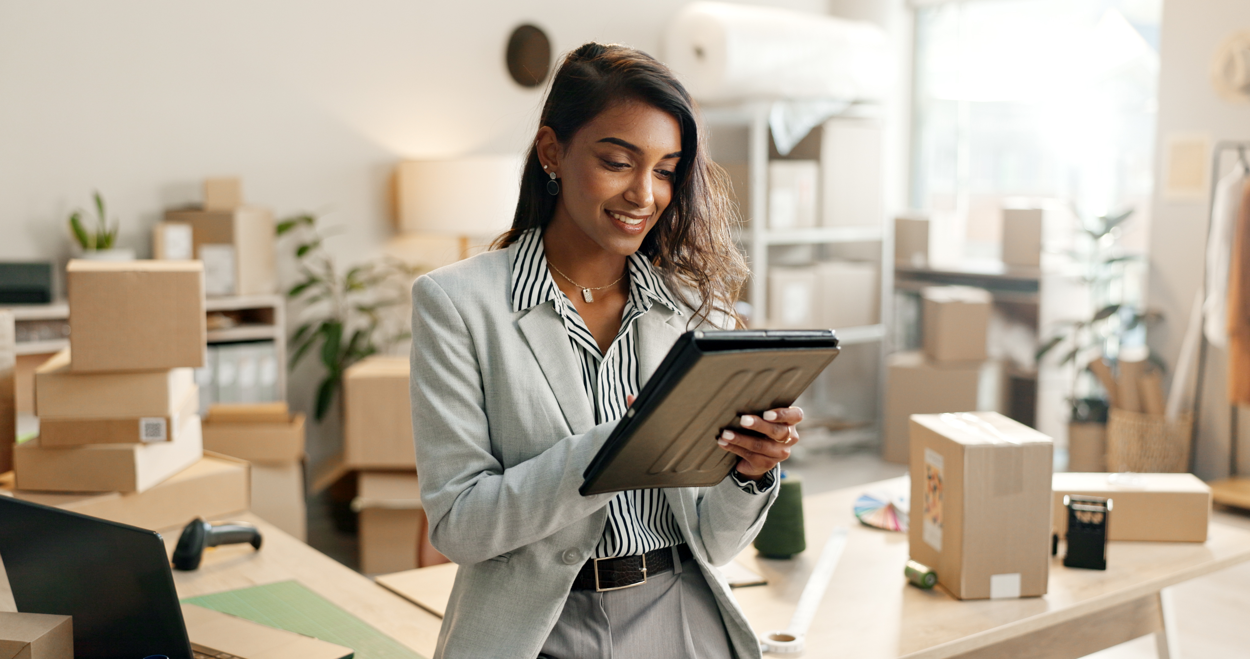 Woman on tablet smiling, she is wearing a suit and surrounded by boxes