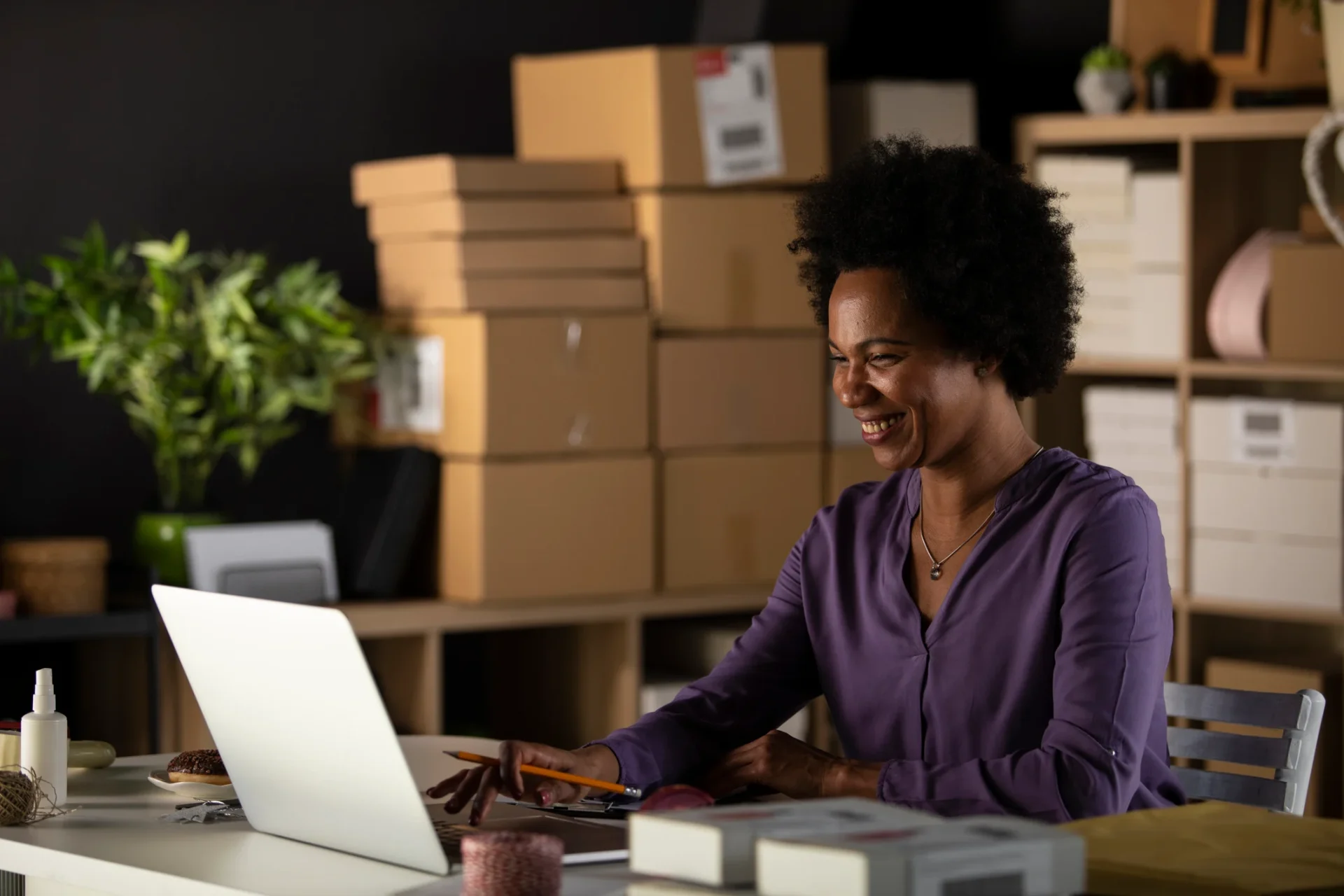 Woman on laptop smiling with parcels in background