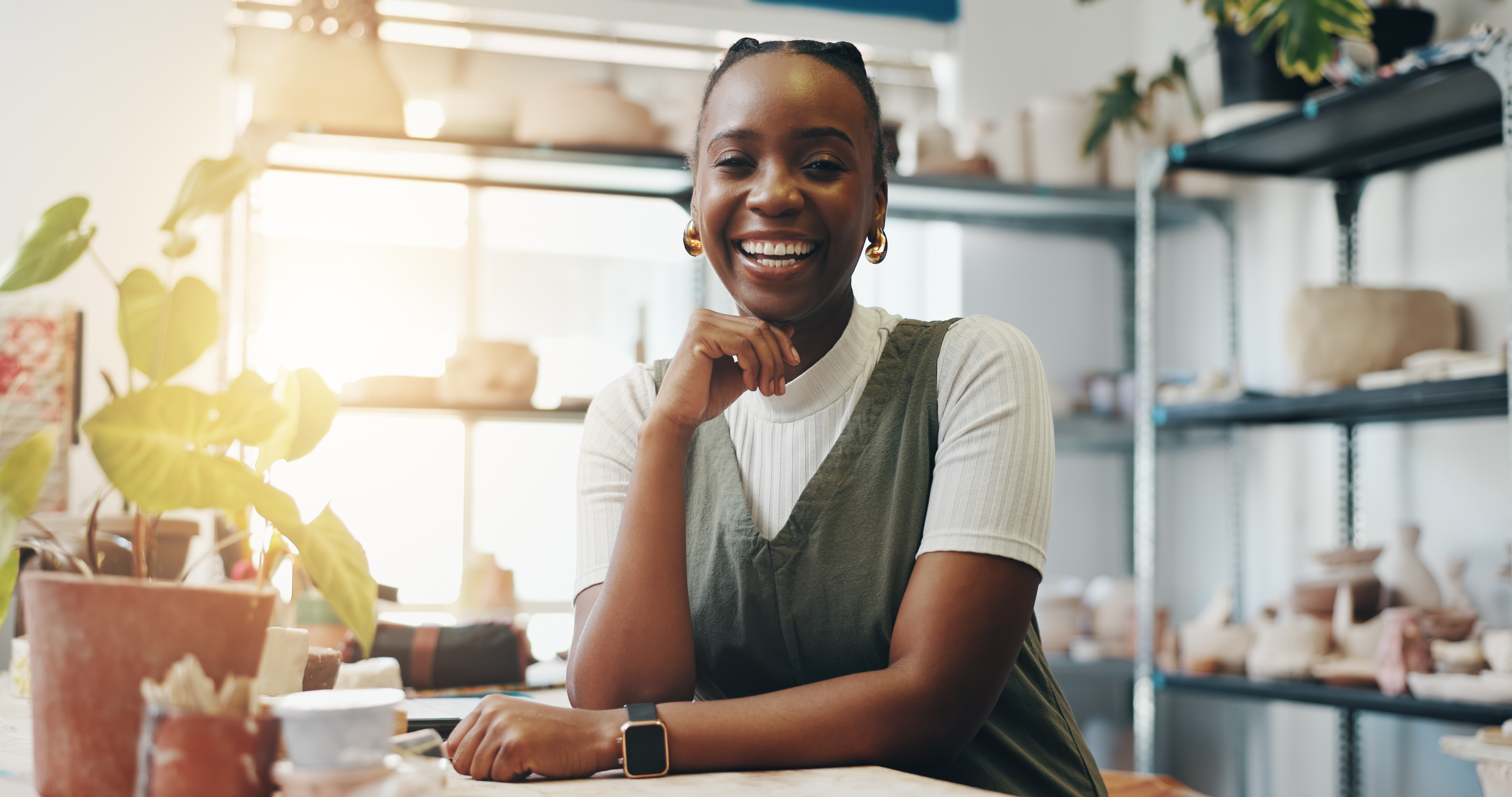 Female presenting person smiles at camera, surrounded by pottery.