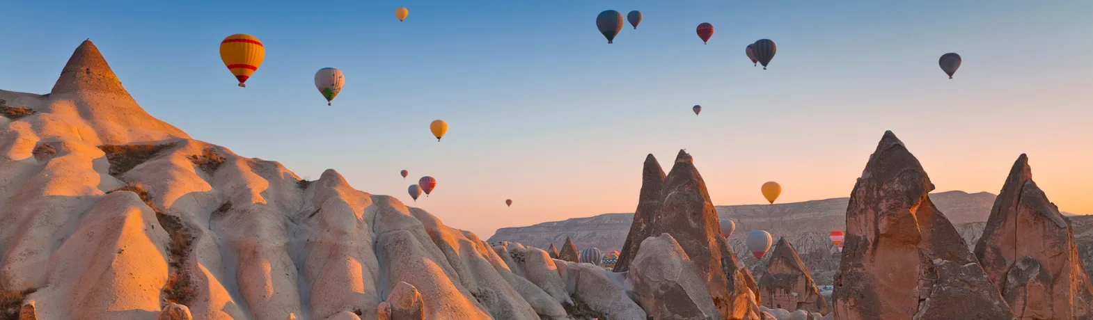 Hot air balloons floating over sandy mountains in Turkey during sunset.