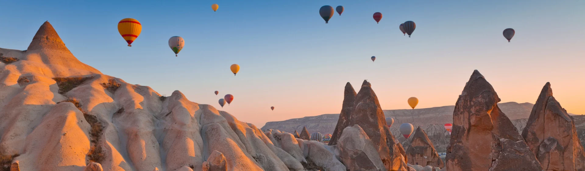 Hot air balloons floating over sandy mountains in Turkey during sunset.