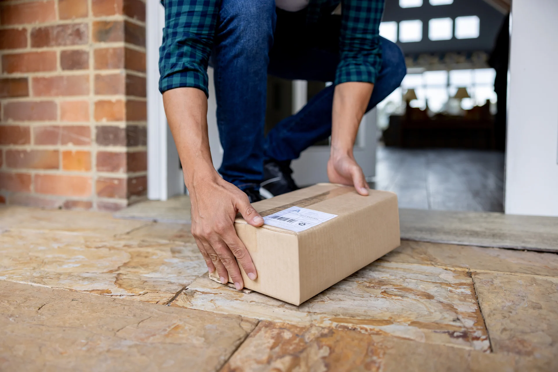 Person crouched down to pick up parcel left on doorstep.
