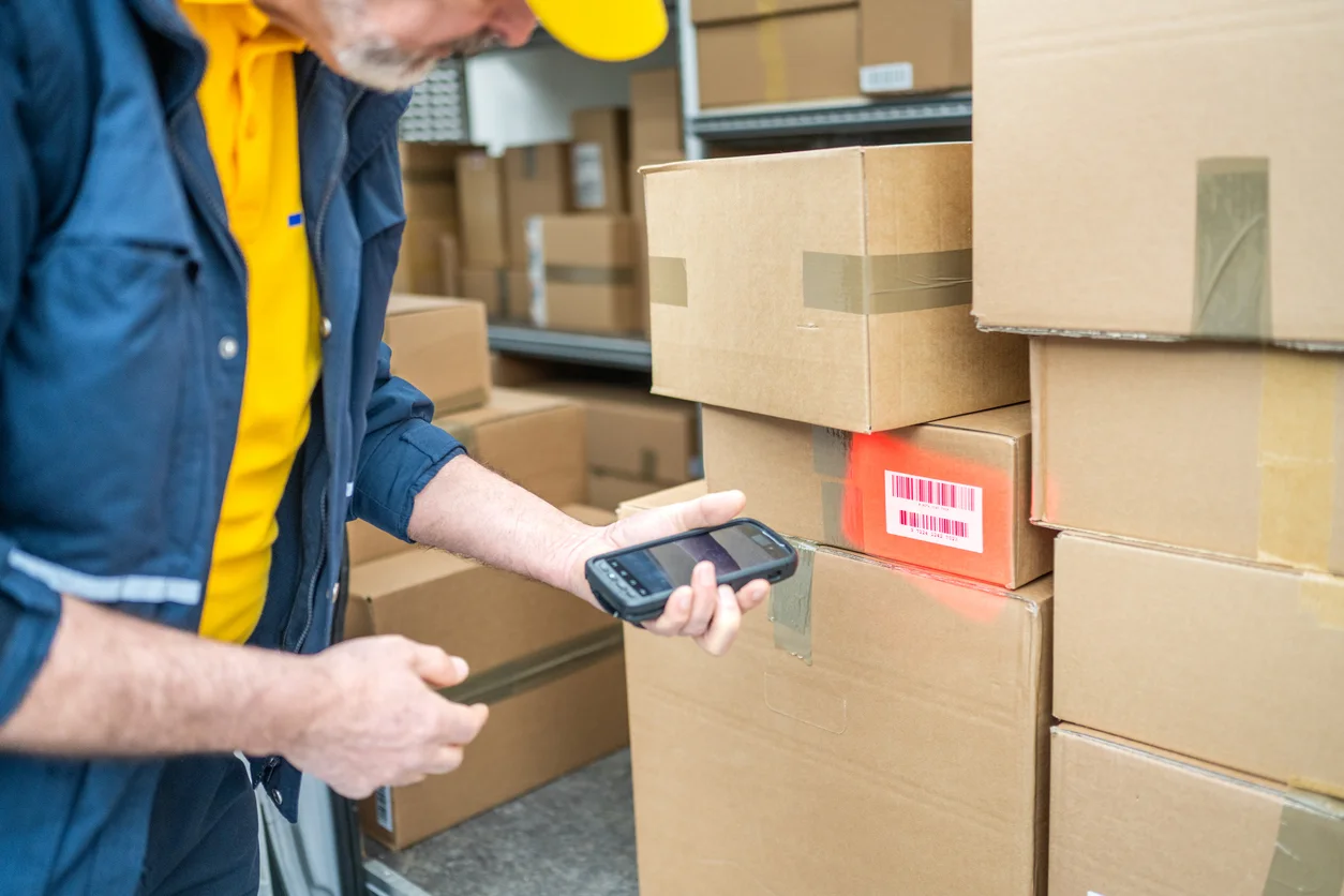 Delivery man scanning label on 1 parcel in a larger stack of parcels