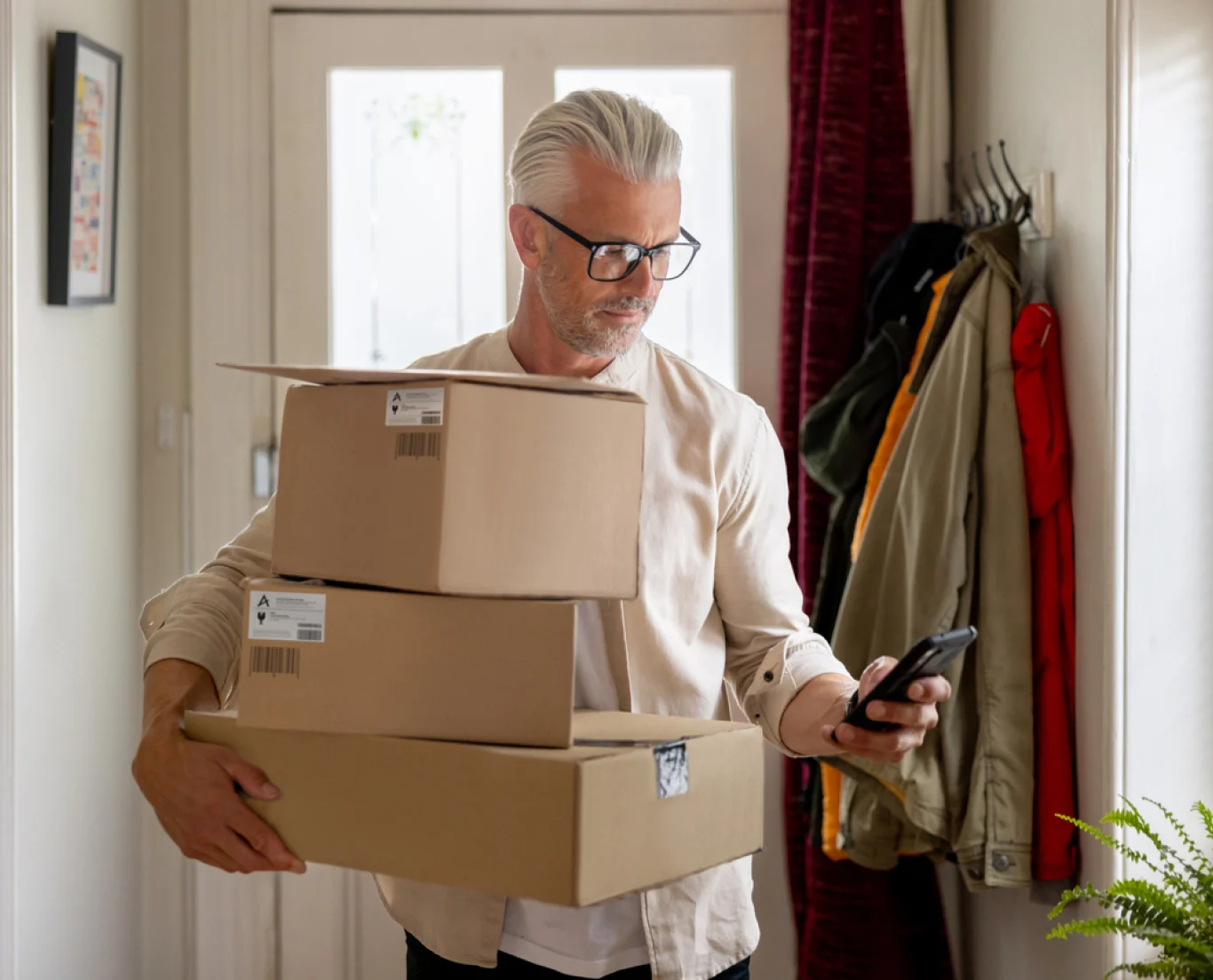 Man holding 3 boxes at home while looking at phone screen