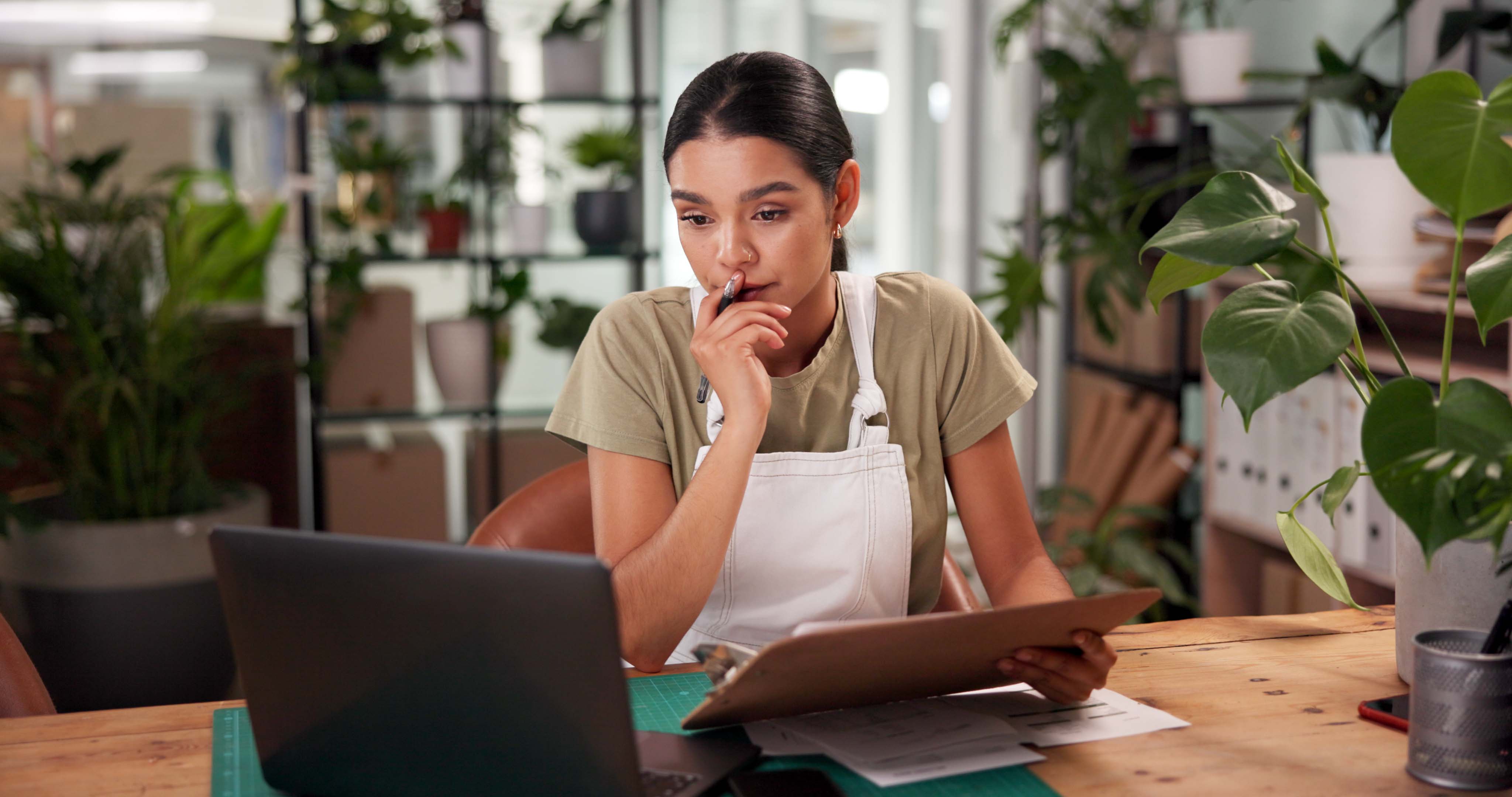 Female presenting person works at her computer in a plant shop.