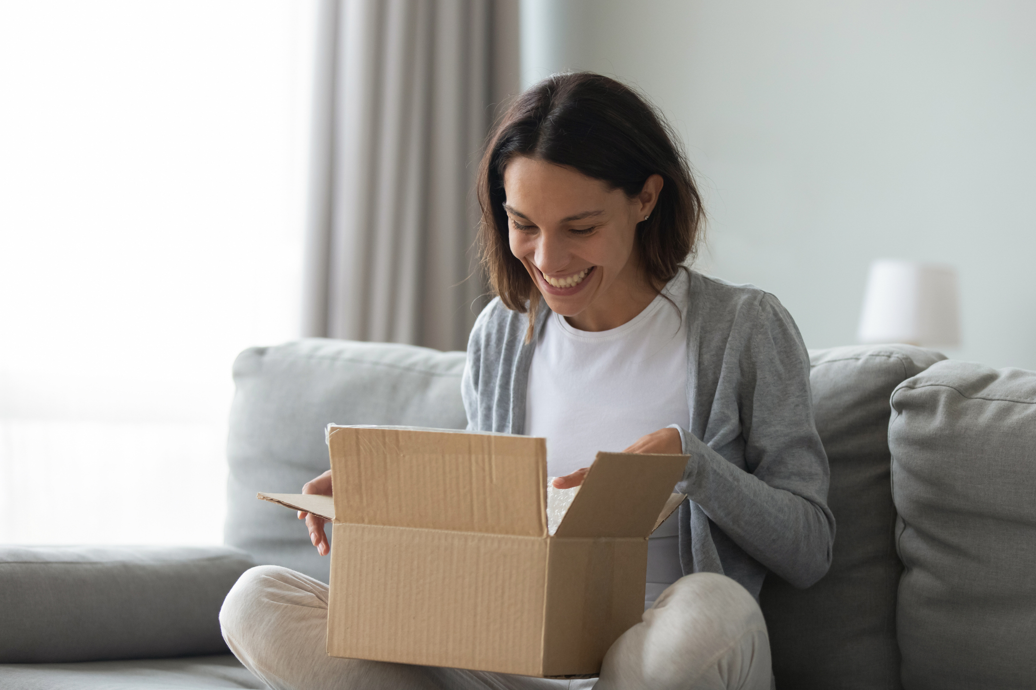 woman opening parcel on couch at home