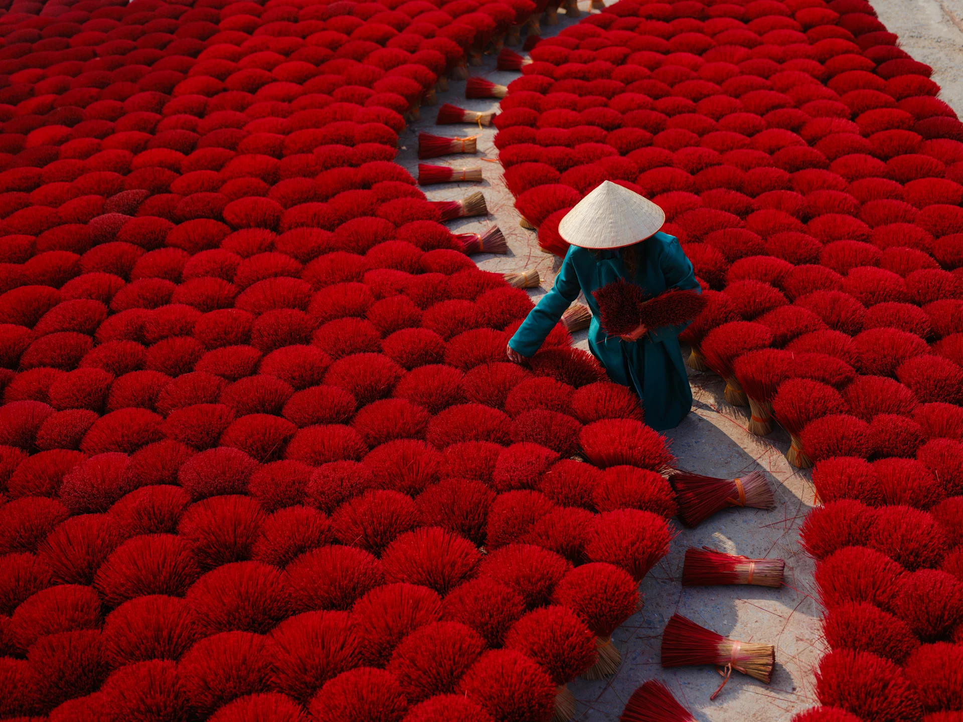 Woman working in incense making village, Vietnam. Wearing a green dress and white hat, surrounded by bunches of red incense.