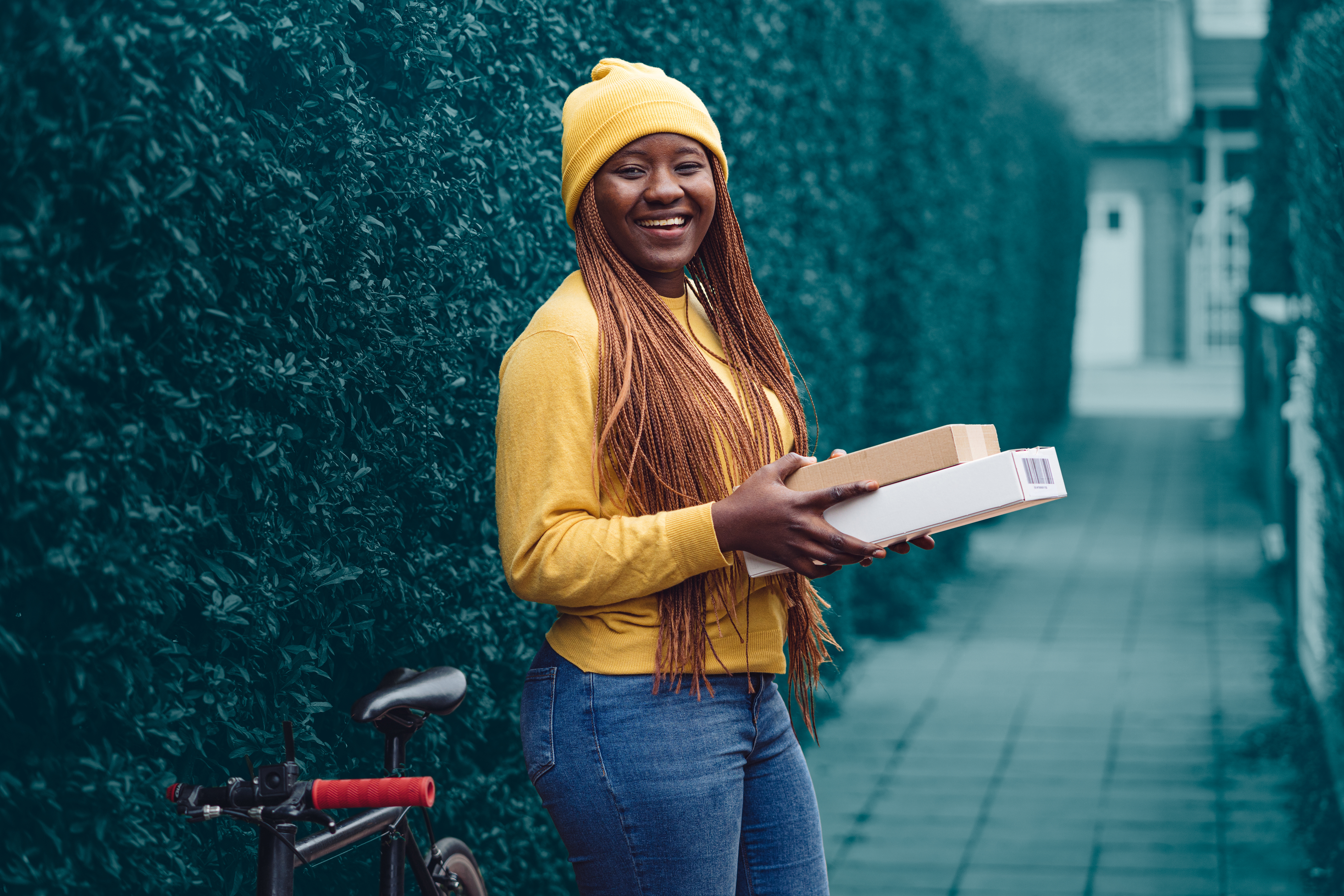 Mujer sosteniendo paquetes y parada junto a su bicicleta, sonriendo a la cámara.