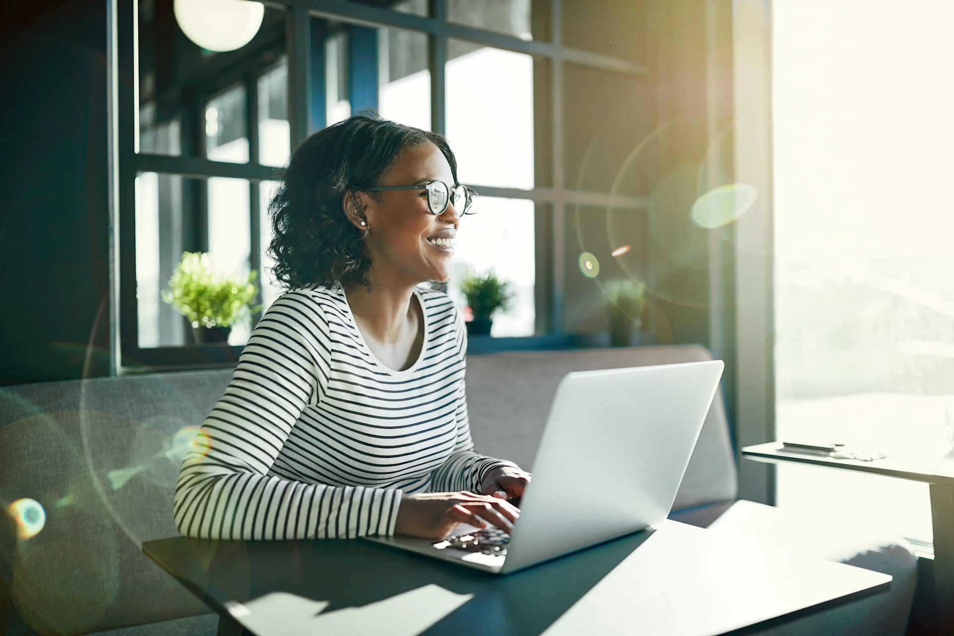 Female presenting person sit's at her laptop in a bright office, smiling.