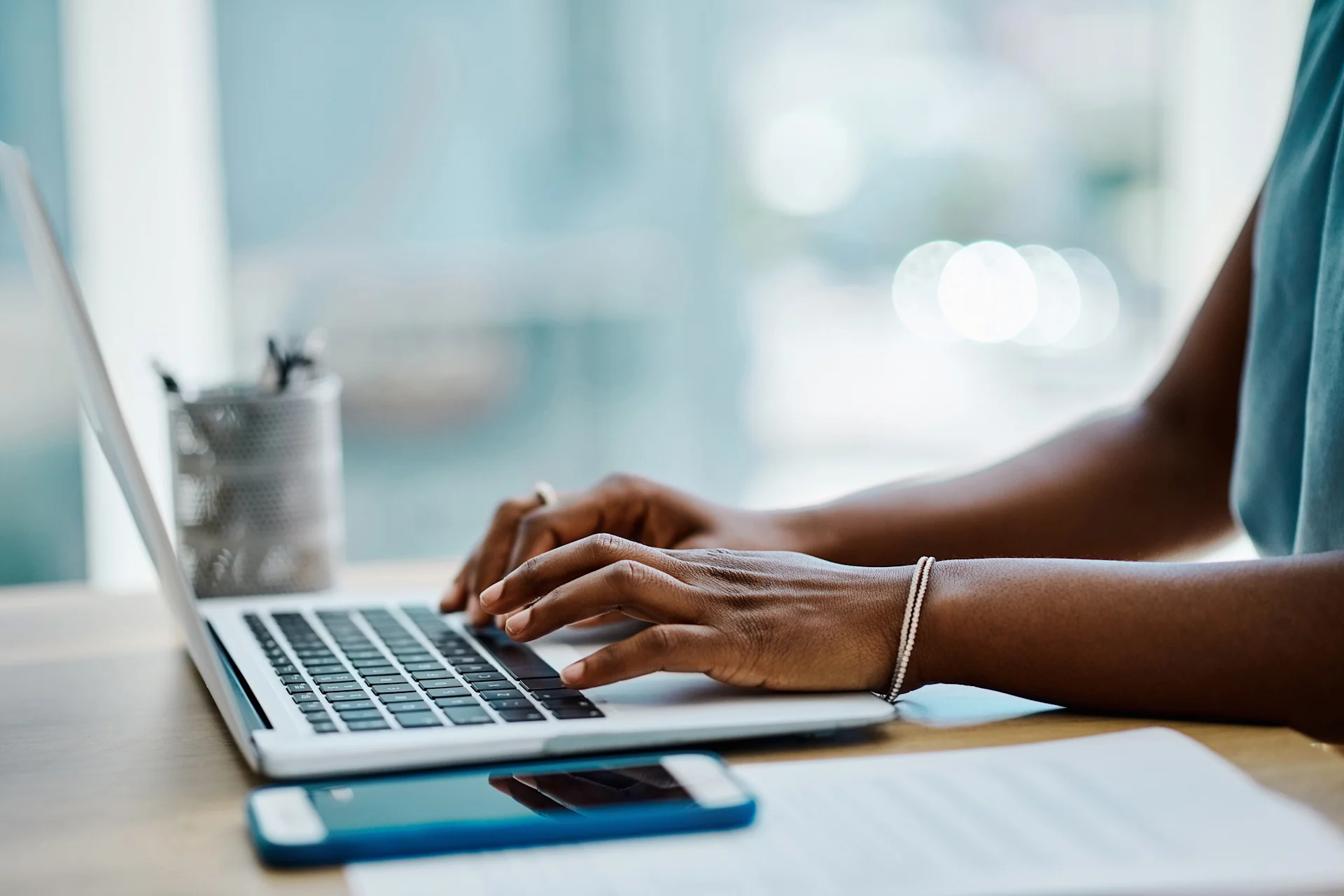 Person's hands typing at laptop by a window