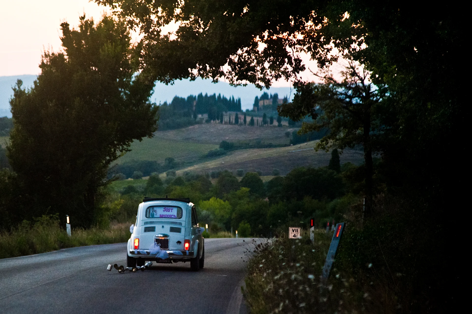 Blue car with cans attached to the back and a sign that reads 'just married'