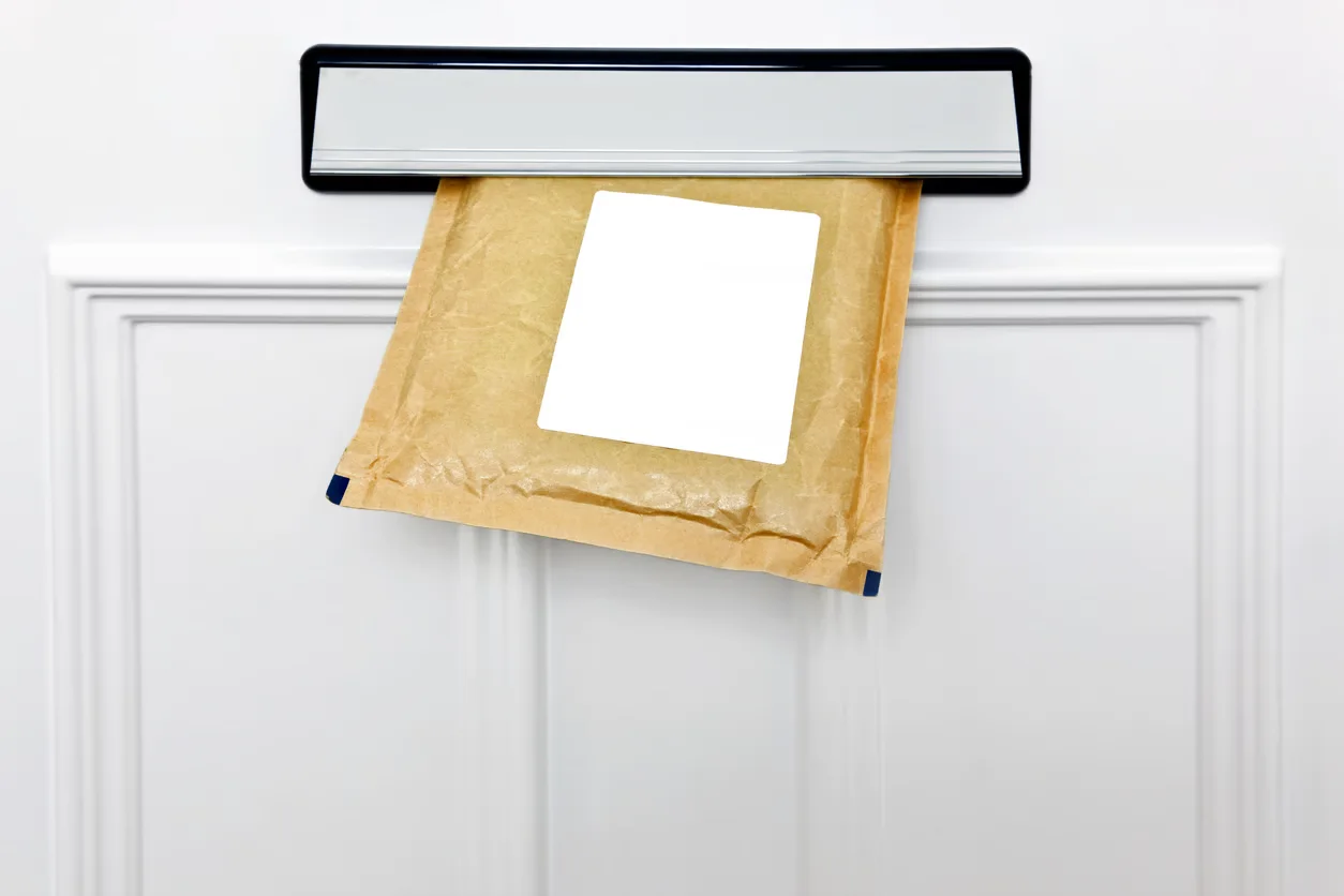 Brown letter sized package half posted through a letterbox