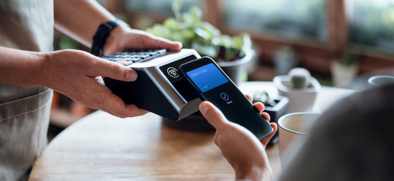 A hand holding a card machine as someone taps their phone 