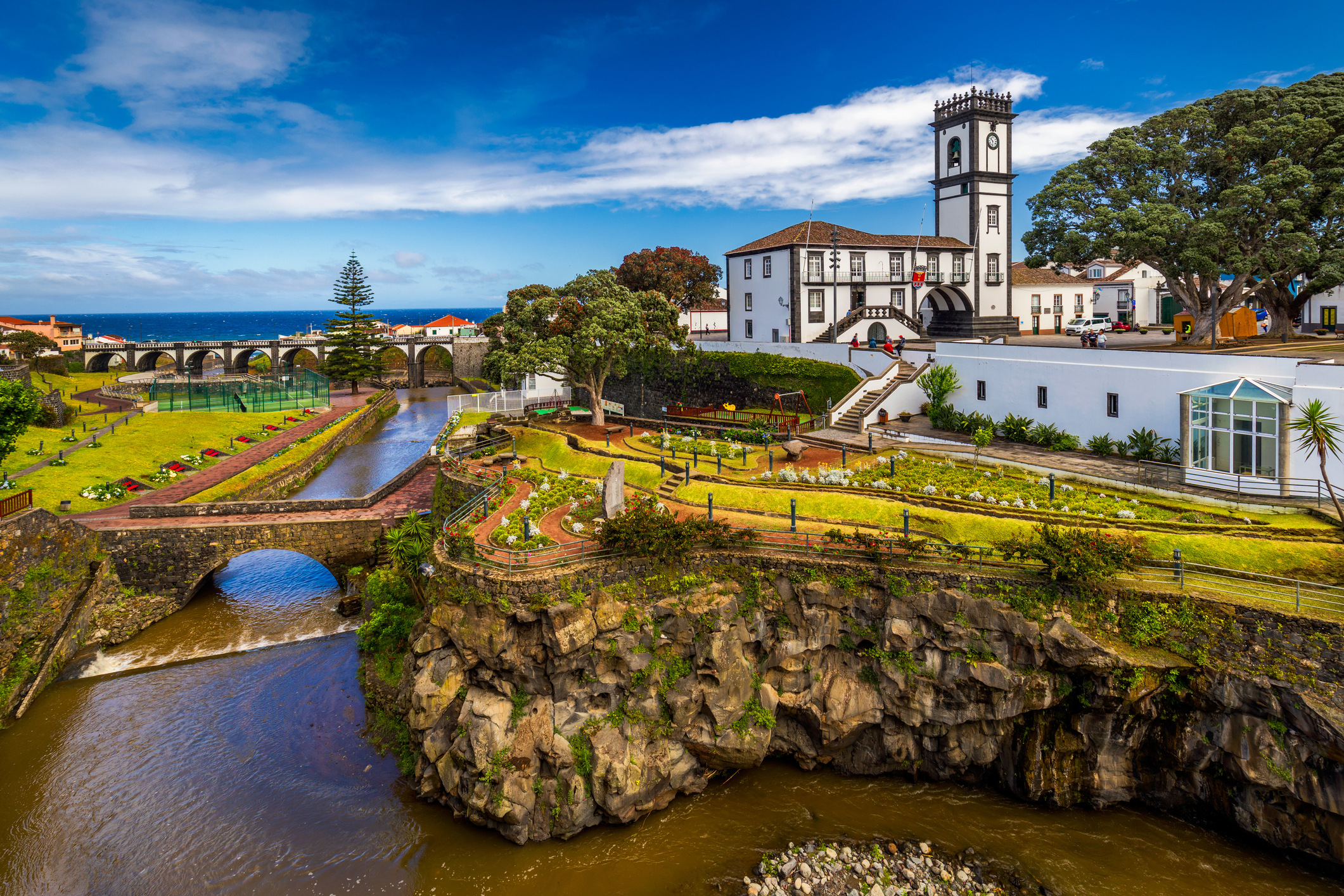 A large white building on a cliff, looking over water and a bridge