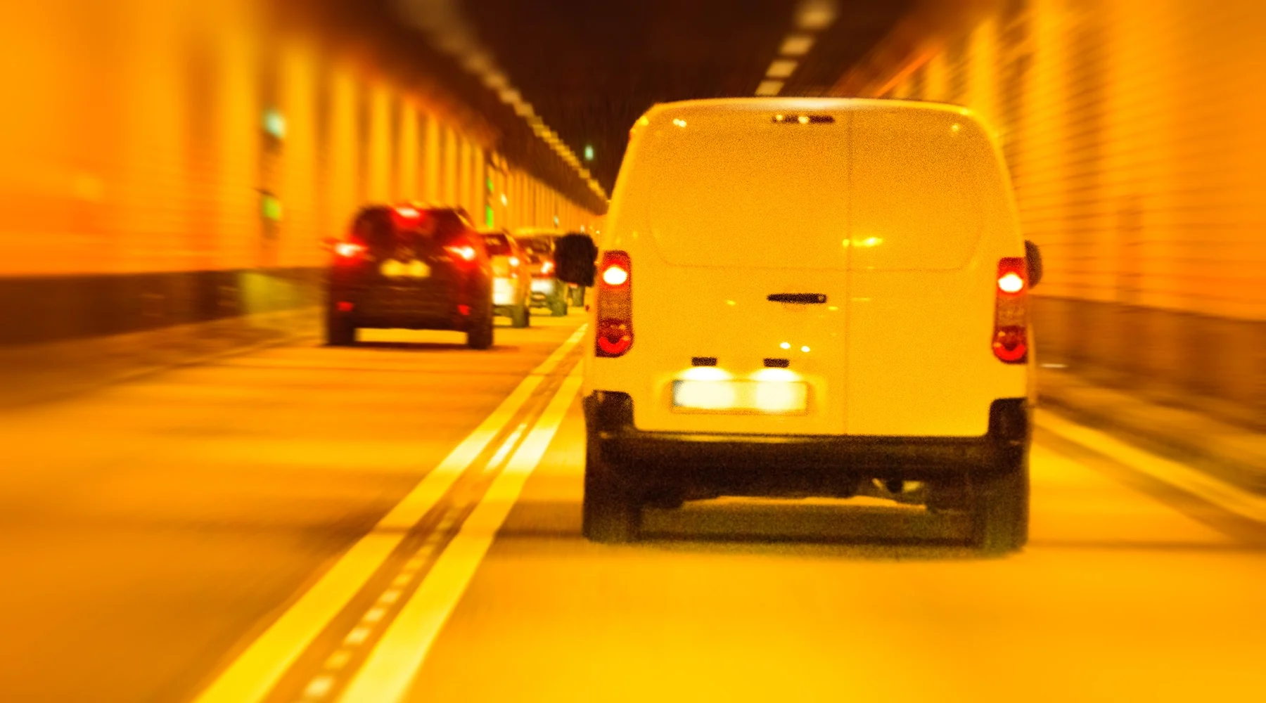 Van from back driving away, lit by orange light in tunnel