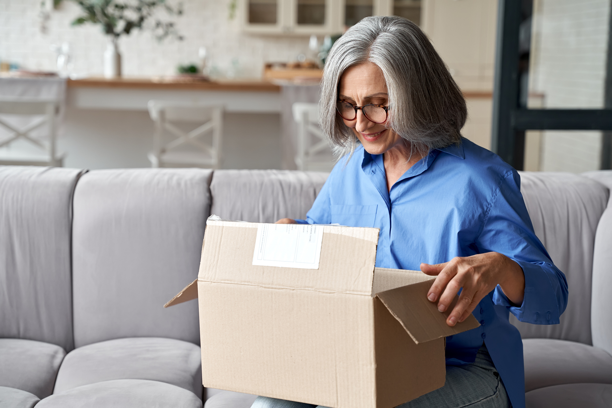 Female presenting woman looking into open parcel box, smiling.