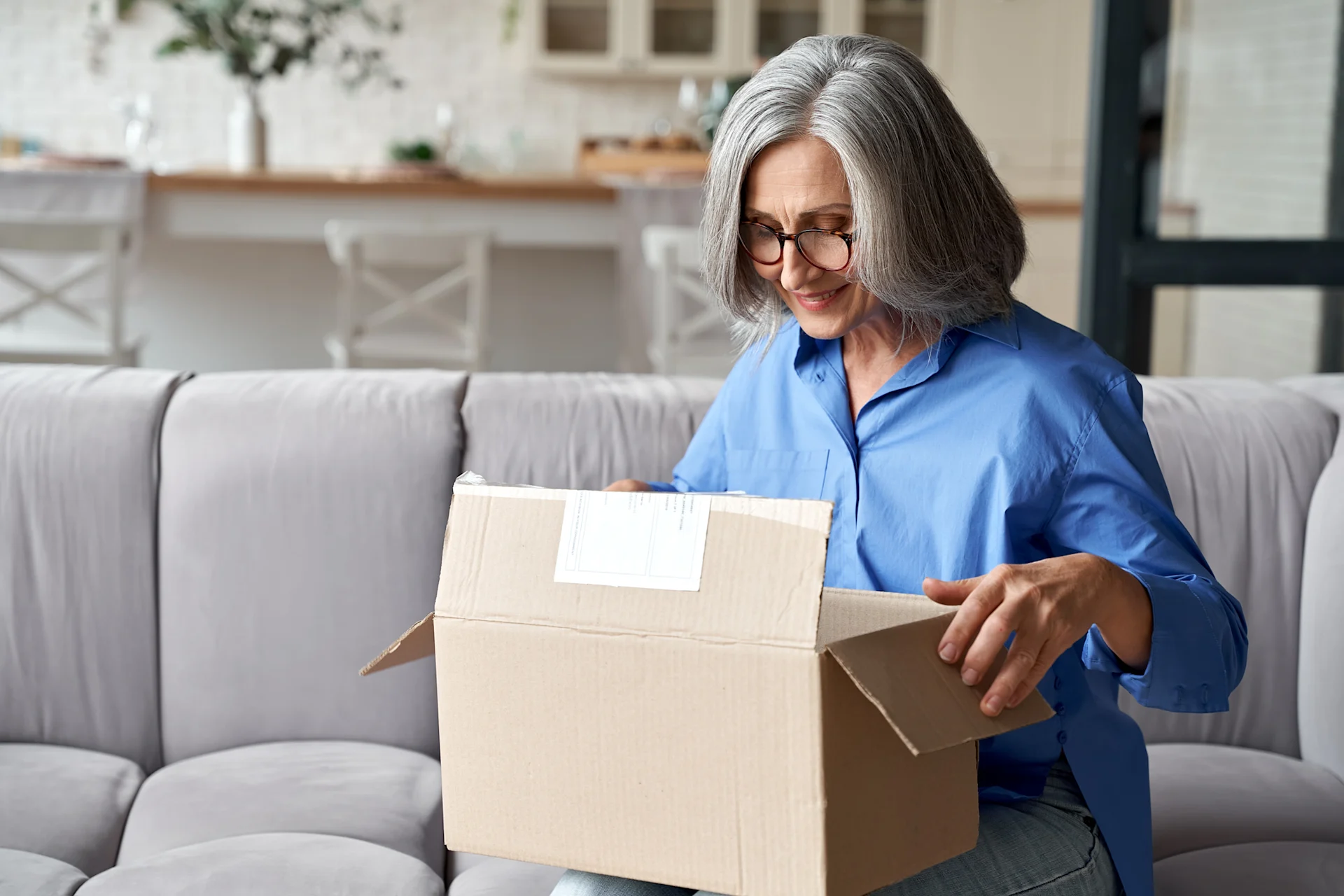 Female presenting woman looking into open parcel box, smiling.