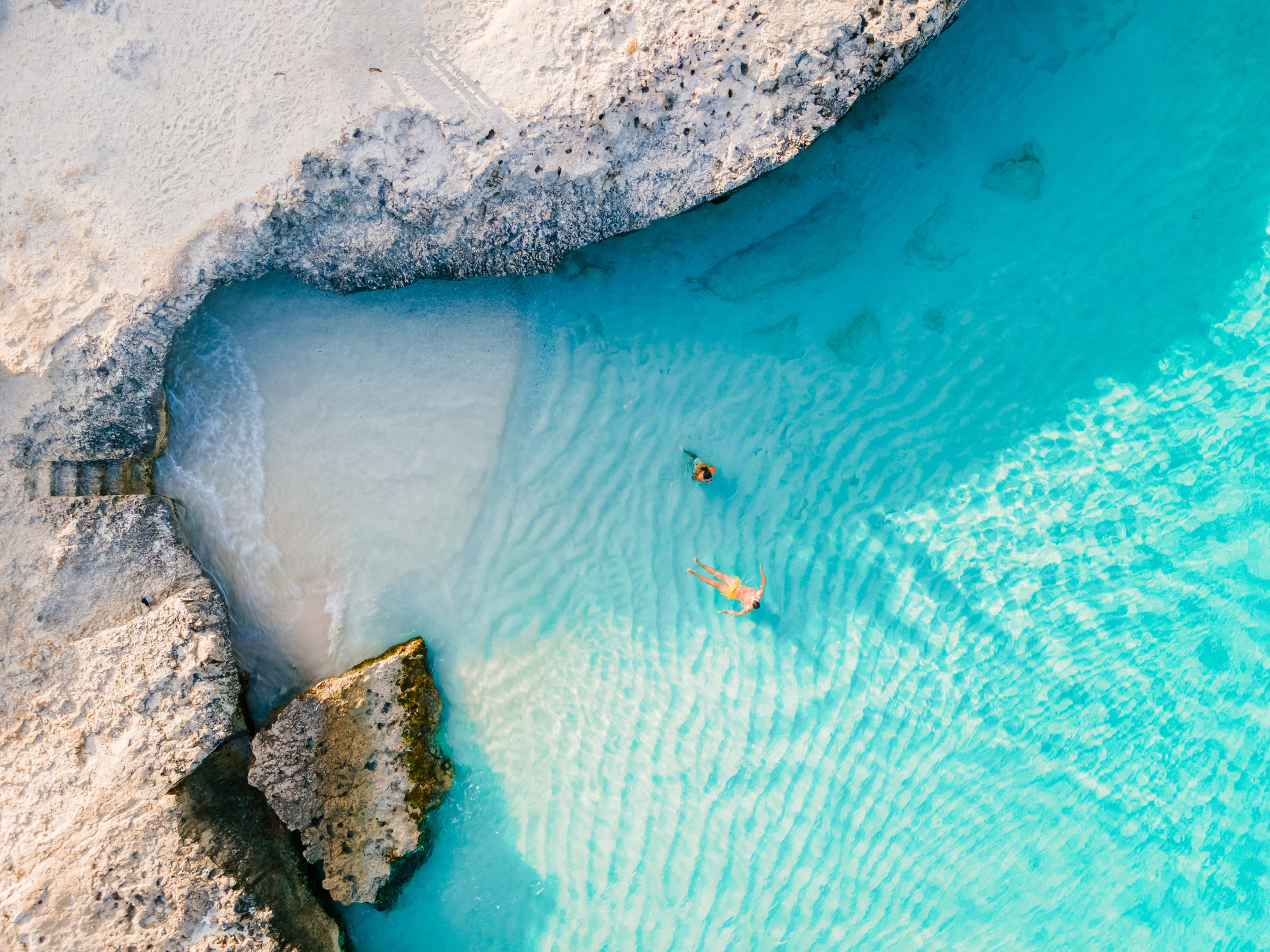 Two people swimming in a vibrant blue cove of water, by a mini beach, in Aruba
