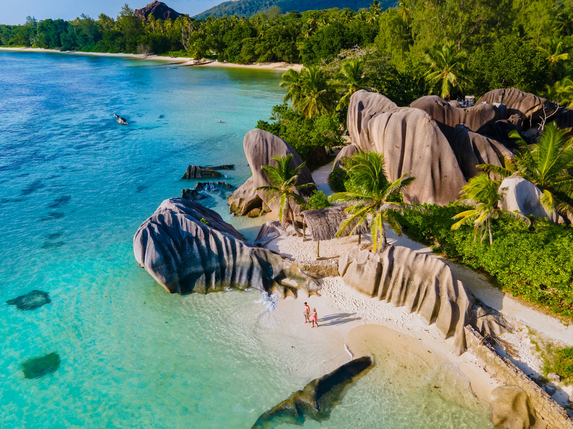 People on an island on Seychelles - clear blue water, unique rocks and vibrant green trees.