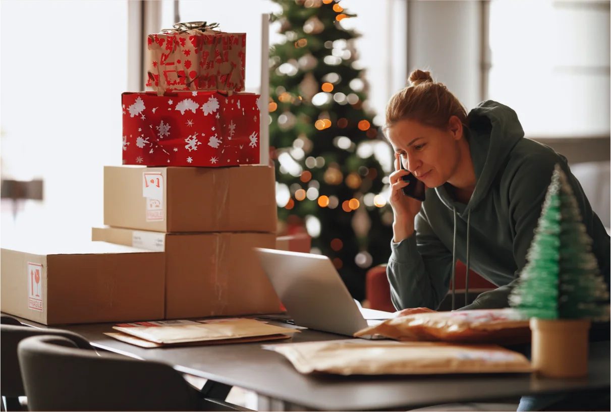 A woman on the phone with a pile of boxes and Christmas present next to her