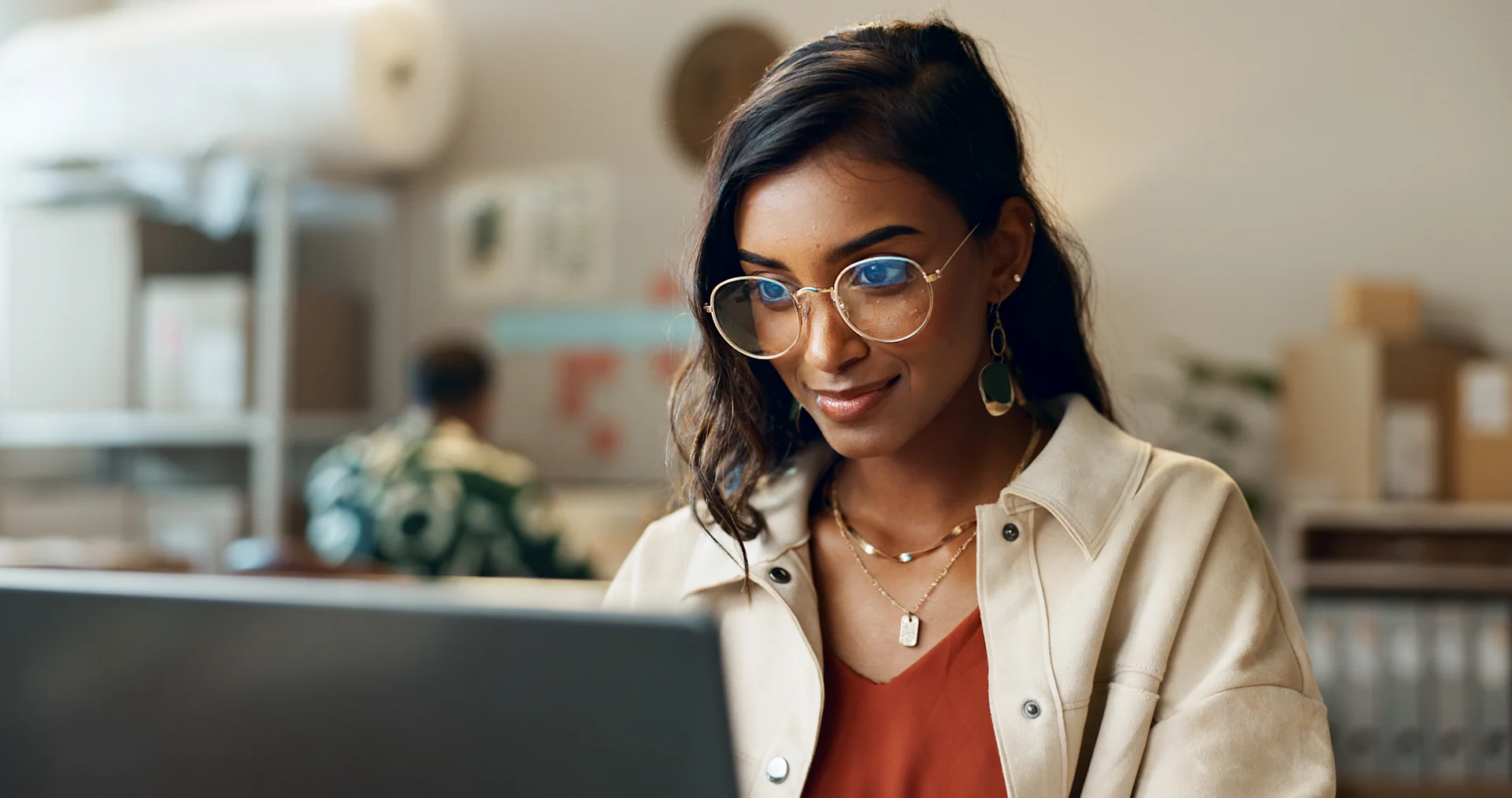 Female presenting person with glasses looks at her laptop screen.