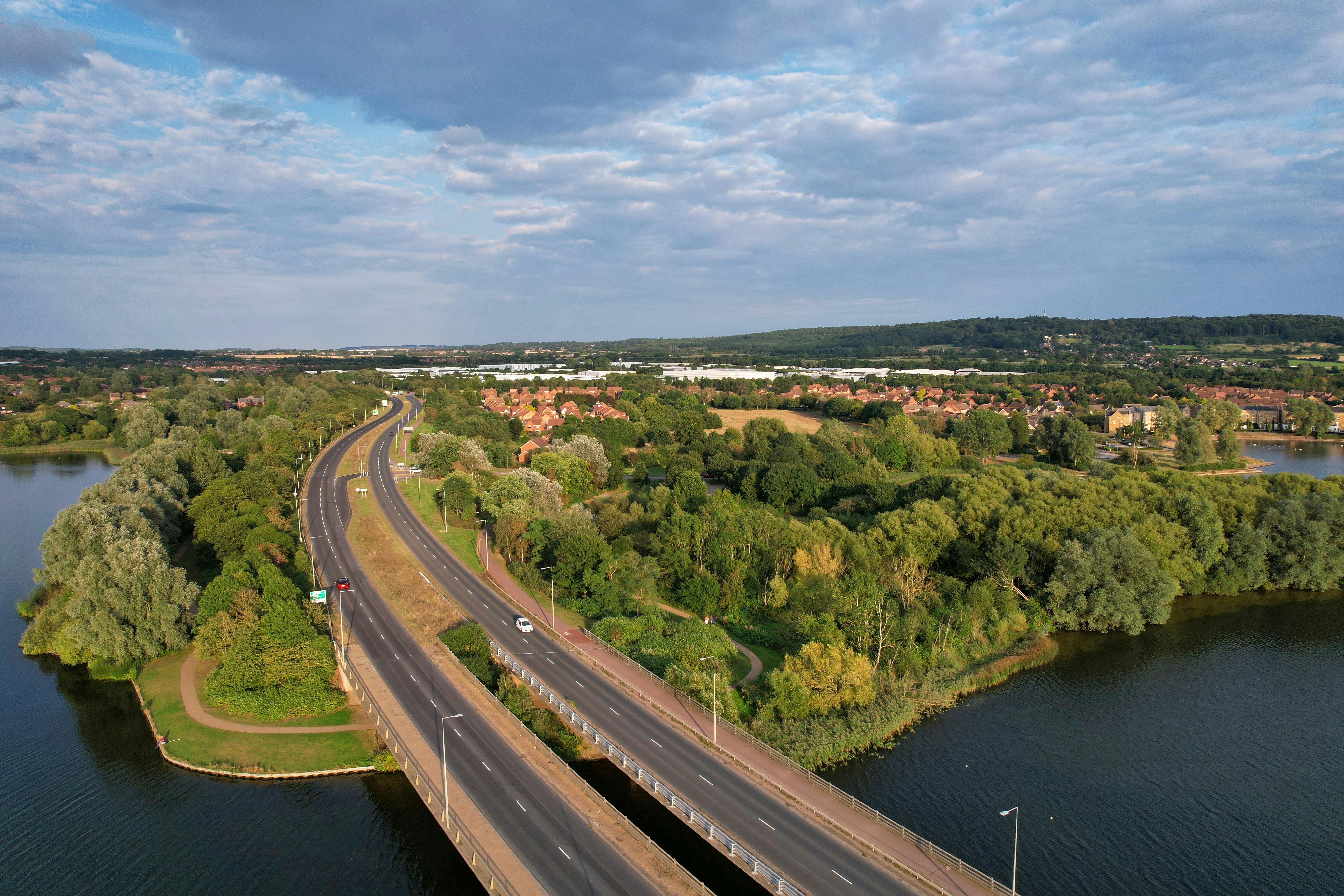 An Aerial Photography of a Road Between Green Trees and River