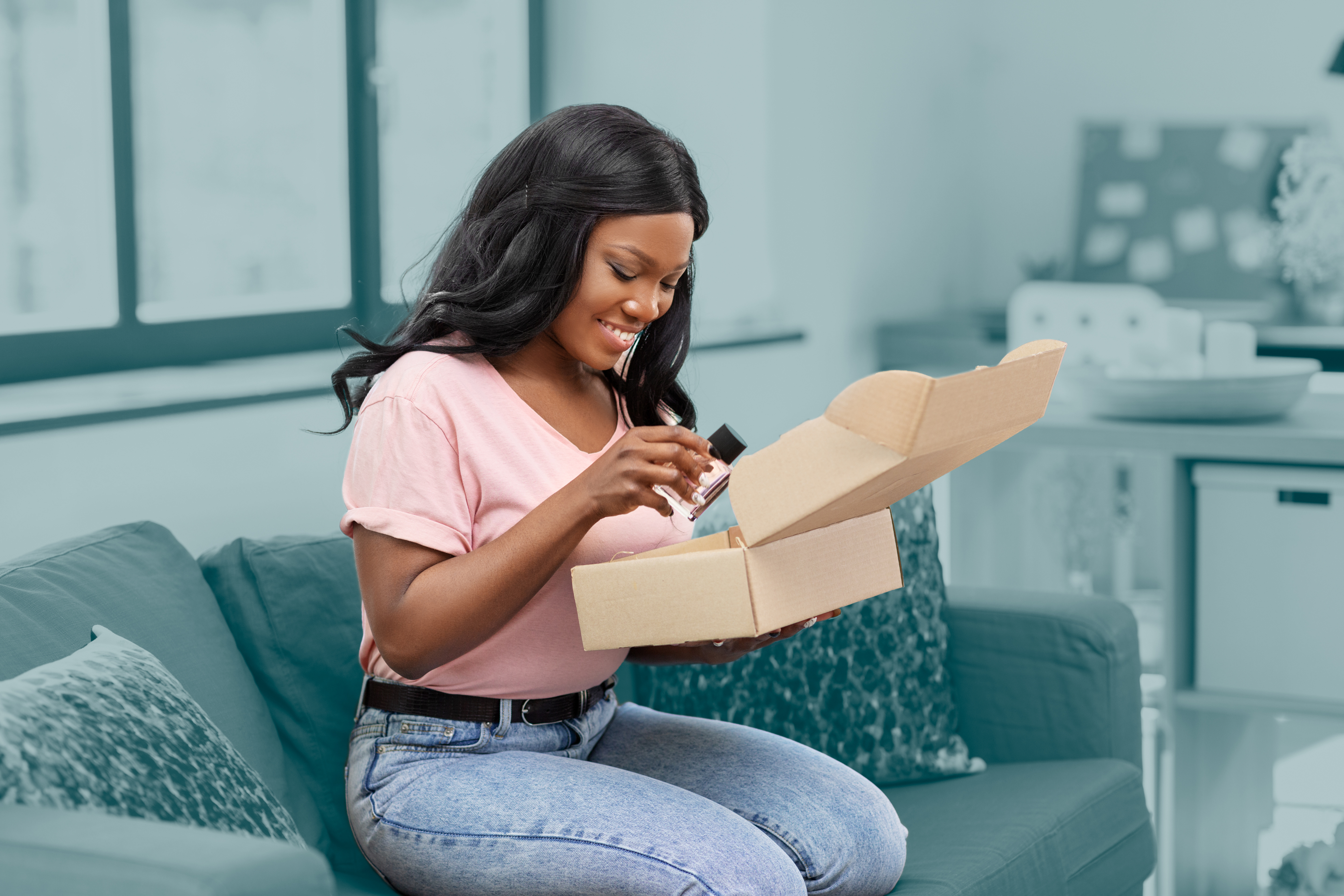 Mujer feliz con camisa rosa, abriendo paquetes en un sofá.